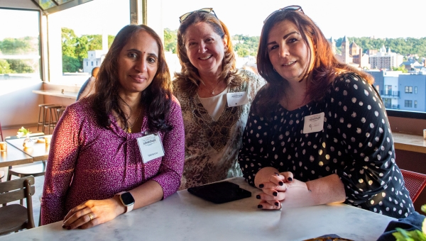 Three Executive Advantage alumni smile at the camera at an outdoor networking event.